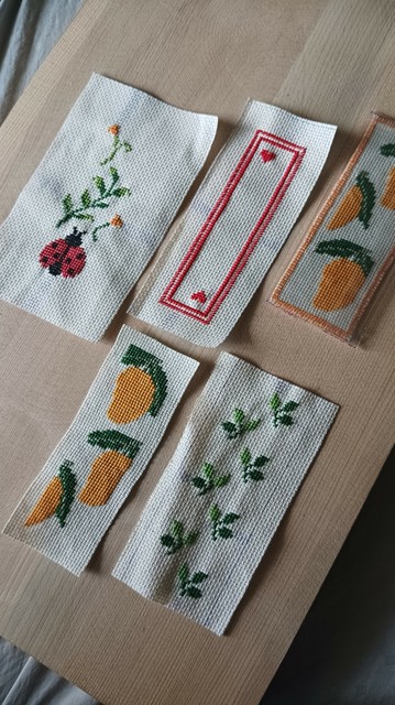 Multiple cross-stitched bookmarks, on a drawing board. 

There's a ladybug and leaves and flower, a simple red double border with 2 hearts. 2 different patterns of mango and one with set of leaves.