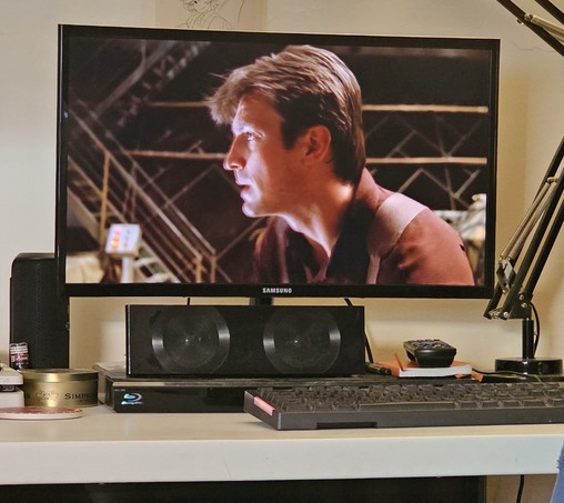 A photo of my computer screen sat atop my messy desk. On the screen is Capt Malcolm from the show Firefly.