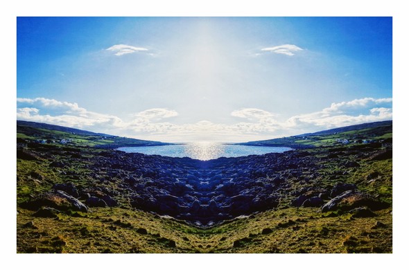 The photo is of the Atlantic ocean taken from the Burren. The photo has been mirrored so each side of the image is a reflection of the other. The bottom portion of the image is a green field with rocks dotted around - the rocks then concentrate in the centre of the image as that's where the shore is. In the middle of the image is the sea which appears like a small round lake because of the distortion causes by the mirroring. On either side of the sea the land slopes down into the sea. There are more rocks and some houses visible which gradually get smaller as you you get further away from the centre. The sky above is bright and blue with some clouds.