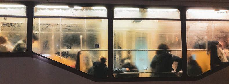 This image shows the inside of a bus or train. The window is foggy, and there are silhouettes of several people seated inside, suggesting it might be crowded or during cold weather. The lighting is warm, creating a cozy atmosphere despite the fogged-up windows.