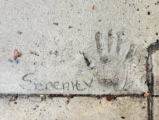 Photo of a hand print in a cement sidewalk. The word "serenity" is inscribed to the left of the hand print.