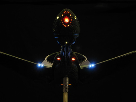 Front shot of a model kit of the Klingon Bird of Prey from Star Trek. Lit with LED lights against a black background.