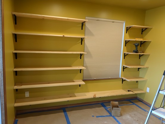 6 runs of pine shelving with black wall brackets. A window sits about 2/3 of the way down the wall.