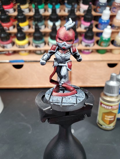 Photo of a partially painted Captain Marvel miniature atop a Citadel painting handle.