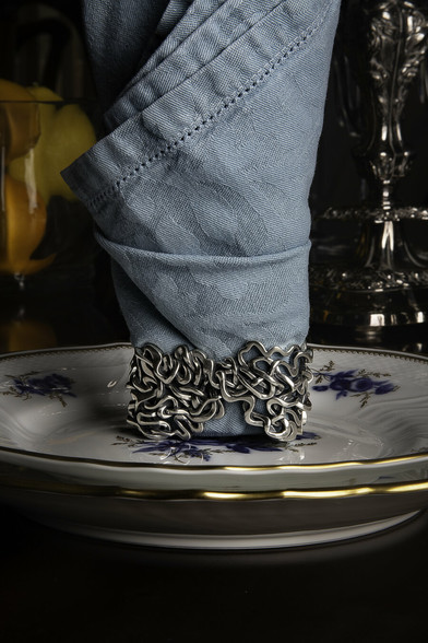 Xover0's solid sterling silver Ancient Courses Napkin Ring is centered on a setting of Ginori china plates. The Napkin Ring holds a robin's egg blue Yves Delorme linen jacquard napkin folded upright in a flame-like shape. A Baccarat vessel of Meyer lemons and an antique sterling silver candelabra set the background.