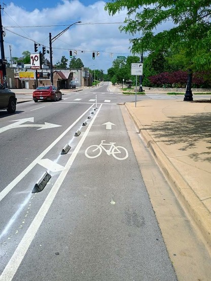 A bike lane at 3rd and Eagleson in Bloomington, IN. It's separated from two lanes of 30MPH one-way traffic by a series of six-inch high rubber barriers.