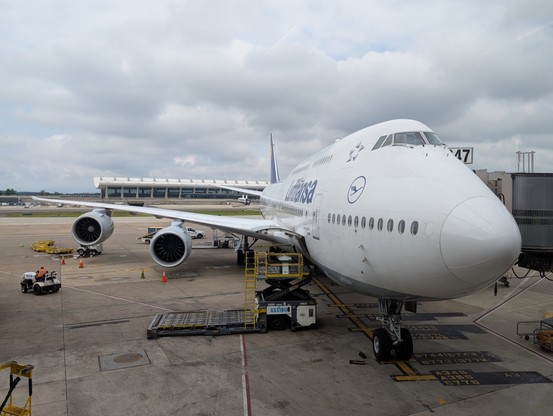 One of Lufthansa's Boeing 747-8 jets sits parked at gate B47 at Dulles Airport, with IAD's main terminal visible behind it.