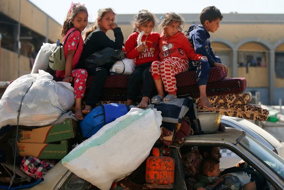 A family flees with their children (four girls and a boy) sitting on the roof of a civilian car and bags of belongings.