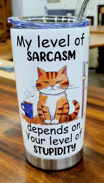 A white coffee tumbler with black text. The tumbler is on a brown tabletop at a store with fuzzy view of objects in the background.

Two lines of text at top of tumbler, cartoon of an orange cat with a blue coffee mug by it, three lines at the bottom of the tumbler.

My level of
SARCASM 

<cat>

depends on
Your level of 
STUPIDITY