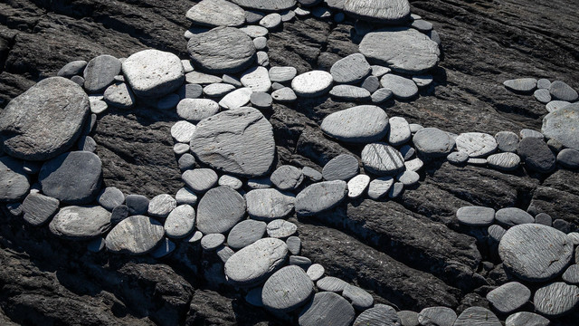 A detail view of an ampersand formed of rounded slate stones, laid on a rock.