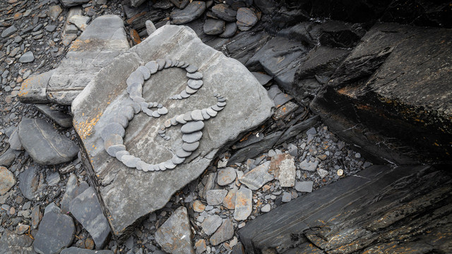 An ampersand formed of overlapping rounded slate stones. On a bigger, flat, rock.