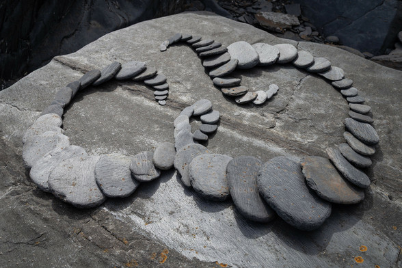 An ampersand formed of overlapping rounded slate stones. On a bigger, flat, rock.