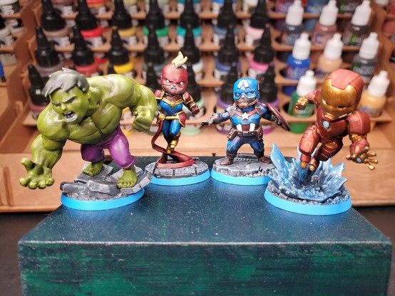 Photo of painted miniature versions of (from left to right) Hulk, Captain Marvel, Captain America (Steve Rogers), and Iron Man sitting atop a green box.