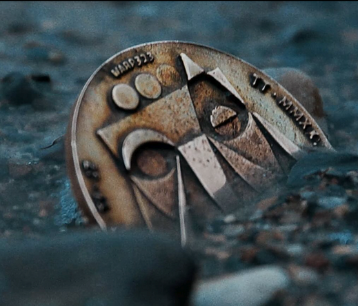 Image of one of the Thom Yorke coins half buried.