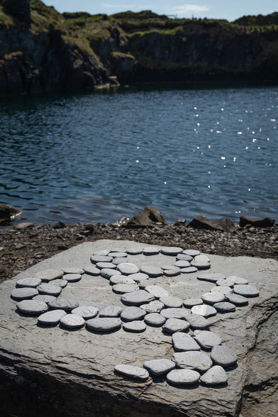 An ampersand on a big square rock. Sunlight sparkles on the still water of the adjacent flooded quarry.