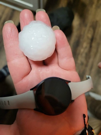 A hand holding a big piece of hail and an Apple Watch. The hail and the watch are about the same size in diameter.