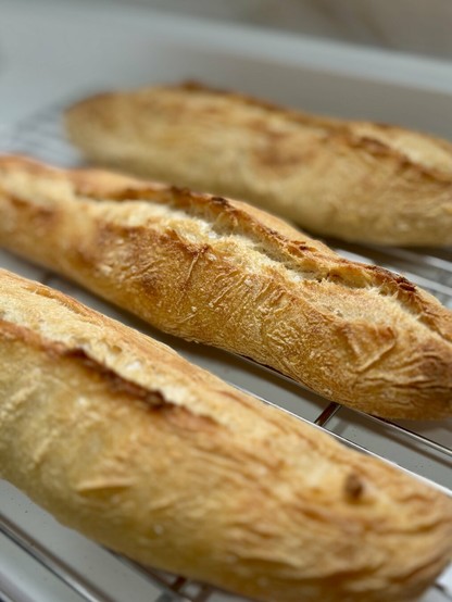 Three freshly baked baguettes cooling on a wire rack.