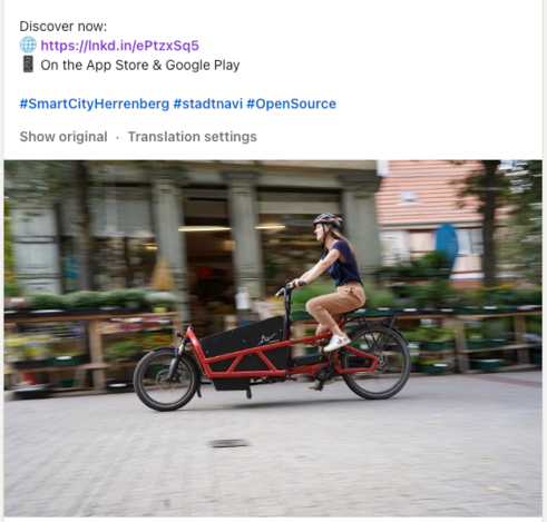 A promotional social media post featuring a woman riding a modern cargo bicycle through an urban street, with the caption encouraging viewers to "Discover now" and linking to an app available on the App Store and Google Play.