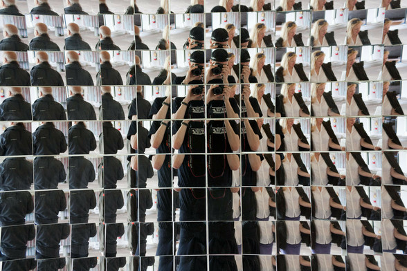 a reflection of a male person in black taking their picture in a set of numerous small mirrors, all angled slightly different, so that the picture looks broken into many little ones.