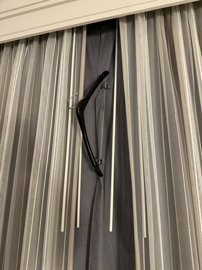 A hotel room window with the blinds held shut using the trouser clips of a clothes hanger.
