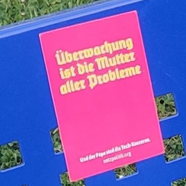 Makroaufnahme des Stickers. Pink und in gelber Runenschrift "Überwachung ist die Mutter aller Probleme"