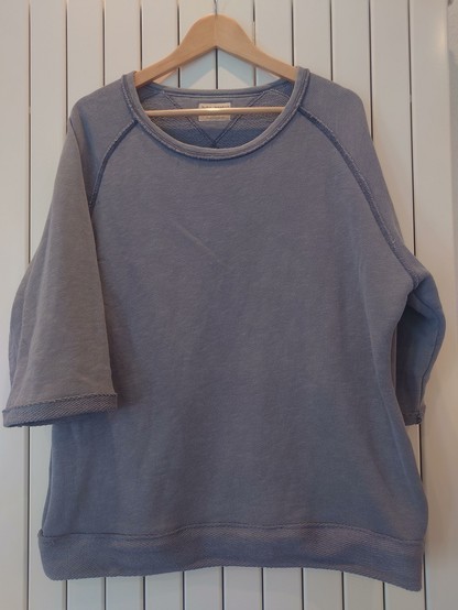 Umgearbeiteter Pulli auf Holzkleiderbügel an einer Heizung. Die Ärmel haben nur noch dreiviertel Länge und alle Säume sind aus dem Pullistoff auf Links.