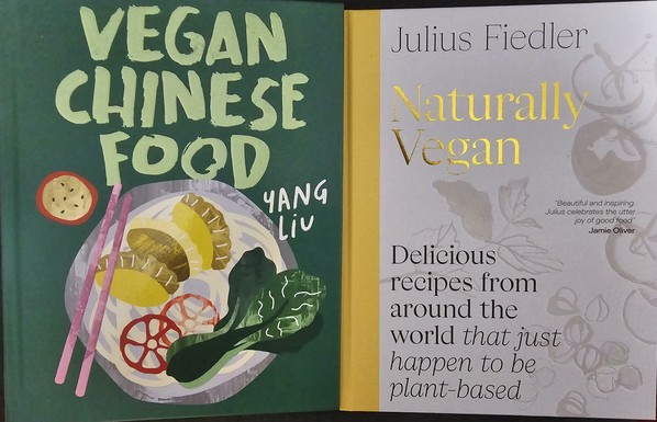 Two books placed side-by-side. Left book is titled 'Vegan Chinese Food' by Yang Liu, the cover depicting vegetables, dumplings, and noodles on a dish with chopsticks. Right book is titled 'Naturally Vegan \ Delicious recipes from around the world *that just happen to be vegan*' by Julius Fiedler (where the asterisks indicate italics), with a quote by Jamie Oliver "Beautiful and inspiring. Julius celebrates the utter joy of good food". The cover depicts vegetables in monochrome.