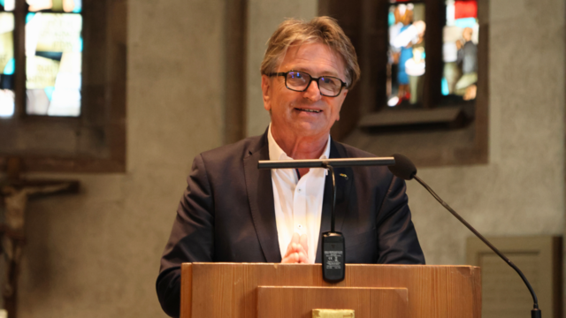 Minister Manne Lucha steht an einem Rednerpult in einer Kirche und spricht.