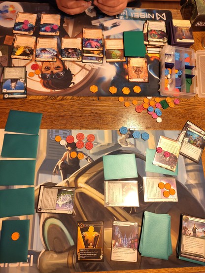 Two playmats full of cards in sleeves, upside down. Many tokens in between and generally looking a bit chaotic
