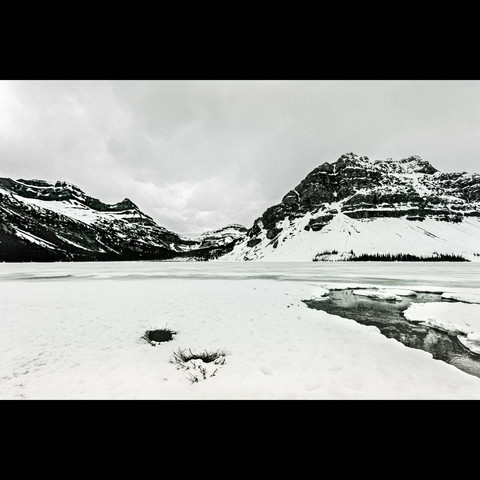 Black and white photo of a mountain and a frozen lake with snow above