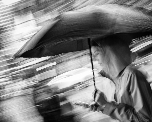 Black and white photo of a woman holding umbrella and phone.