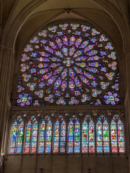 Ein Fenster von Notre Dame. 

KI, überarbeitet : Das Bild zeigt die beeindruckende Innenausstattung einer gotischen Kathedrale, insbesondere einen großen, runden Rosettenfenster und eine Reihe von hohen, schmalen Fenstern. Das Rosettenfenster, das sich über die gesamte Höhe des Bildes erstreckt, ist ein Meisterwerk aus farbenfrohem Glas, das in einem komplexen Muster aus Kreisen und Blütenblättern angeordnet ist. Die Farben sind lebendig und reichen von Blau und Rot über Grün und Gelb bis hin zu Violett, und die Details sind sorgfältig gestaltet, um eine harmonische und spirituelle Atmosphäre zu schaffen.

Unterhalb des Rosettenfensters befinden sich weitere Fenster, die in hohen, schmalen Reihen angeordnet sind. Diese Fenster zeigen Figuren und Szenen, die wahrscheinlich biblische oder heilige Figuren darstellen, und sind ebenfalls aus farbenfrohem Glas gefertigt. Die Fenster sind mit kunstvollen Ornamenten und Inschriften verziert, die die Geschichte und die Bedeutung der dargestellten Figuren erzählen.

Die Architektur der Kathedrale ist typisch für die gotische Bauweise, mit hohen, spitzen Bögen und einem hohen Gewölbe, das die Fenster umrahmt. Die Fenster lassen das Licht in die Kirche strömen, was die Farben und Details noch lebendiger erscheinen lässt. Die gesamte Szene vermittelt ein Gefühl von Ruhe und Spiritualität, und die kunstvolle Handwerkskunst der Fenster ist ein Zeugnis der künstlerischen und religiösen Traditionen der Vergangenheit.