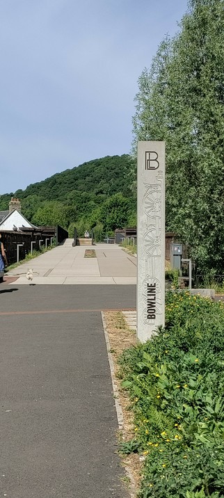 A walkway over a restored disused railway bridge. There is a forested hill in the background A tourist information post brands the walkway "Bowline"