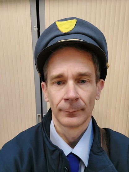 Selfie en postier casquette bleue comme couvre chef, cravate, chemise, veste bleue et sacoche de cuir en bandoulière.