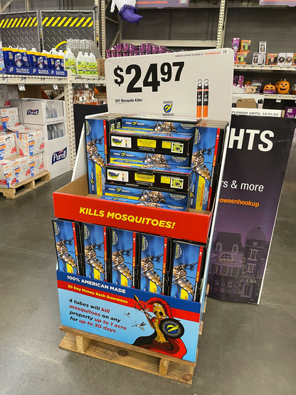 Store display of boxes of Spartan Mosquito Pro Techs, with various claims such as "kill mosquitoes on any property up to 1 acre for up to 30 days" and "100% American made." Each box has a photograph of a mosquito on it. $24.97 per box.