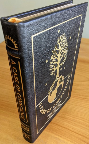 Exquisite Collector's Edition copy of: A Case of Conscience by James Blish from The Easton Press's Masterpieces of Science Fiction Collection, meticulously maintained by a single owner in a private collection, stored carefully in dust-free bookcases in a dry climate. Bound entirely in rich, black genuine leather, the volume is adorned with exquisite original artwork by Ellen Sull Farley, precisely accented in brilliant 22kt gold detailing
 - 
The front cover prominently features a striking illustration in 22kt gold foil depicting a detailed, symbolic image: a tree flourishing upward into branches, rooted deeply within a globe representing Earth, encapsulating the profound ethical and existential themes explored in the novel. Tiny golden stars surround the central design, adding elegance and cosmic depth to the artwork
 - 
The spine, luxuriously hubbed, displays the title A CASE OF CONSCIENCE and the author JAMES BLISH prominently in gleaming 22kt gold lettering, accompanied by intricate decorative motifs at both the top and bottom
 - 
Printed on archival-quality acid-neutral paper to ensure longevity, the pages feature 22kt gold gilded edges that complement the gold accents of the cover. Expert craftsmanship includes traditional smyth-sewn binding and concealed muslin joints, providing exceptional durability. The volume contains a pristine, untouched bookplate inside the front cover and features an introduction by Walter E. Meyers. Flawless, pristine, unread, and as new