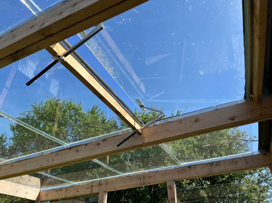 A hinged piece of greenhouse glass, held open by mechanical, temperature controlled pistons.