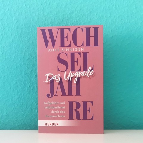 Auf dem Foto ist das Buch "Wechseljahre. Das Upgrade" zu sehen. Es steht vor einer türkisen Wand auf einer hellen, glatten Oberfläche.