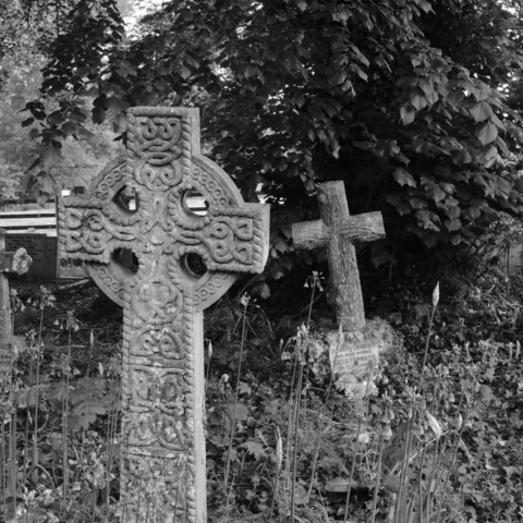 Pictish type cross with circle and patterns. Behind is a wooden style cross. Both made in stone.