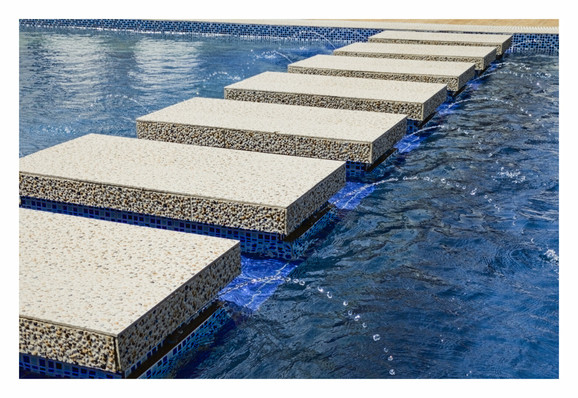 A swimming pool with a series of stepping stones spanning across it. The stones have small fountains integrated within it that spew water right and left.