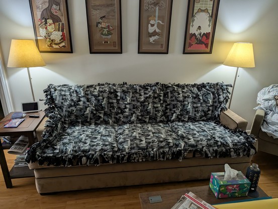 A fleece blanket with tied fringe wedge and wolfs howling at the moon on a beige couch.