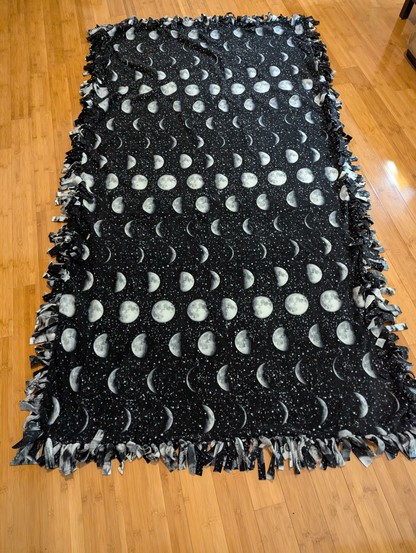 The backside of the larger couch cover blanket with a tied fringe edge and repeating moon phases.