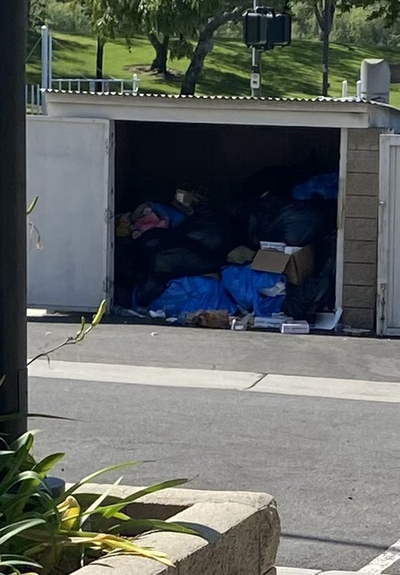 An enclosed trash area with doors open shoeing no dumpster inside just pikes of trash bags