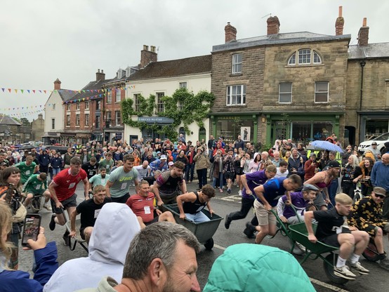 Road closed off and people lining the route. Brave souls are racing past in Wheelbarrows.