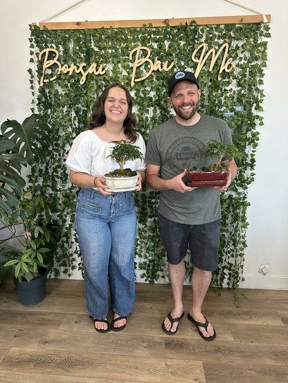 My sister and I proudly holding our new little bonsai creations in front of a wall of green for a photo op at Bonsai Bai Me in Pleasant Grove, Utah.