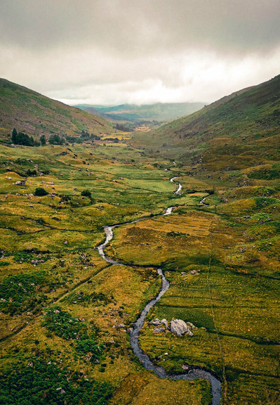 A long river twisting through a green and brown valley with gloomy skies above.