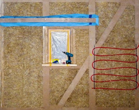 Foto of a straw timber module from a workshop 10 years ago with features like window reveal insulation, airtightness paper and plasterable materials over timber and protruding elements, exemplary heating pipes ready for plaster.