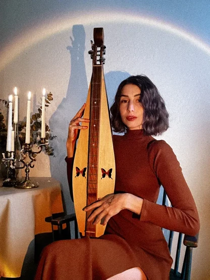 A press shot of meka the folk, singer songwriter holding what looks like a type of lute