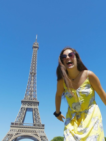 Emily Grice on right in yellow sundress laughing. Picture taken from prone position on ground looking up at model. On left is the Eiffel Tower.