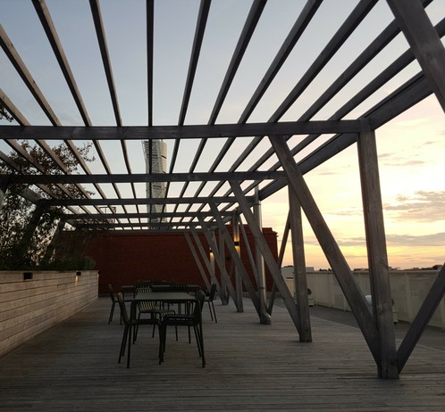 Eine Dachterrasse mit Holzgerüst. Darunter steht eine Tischgruppe. Im Hintergrund geht die Sonne unter. Der Turning Torso schaut hinter einer Wand hervor.